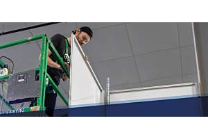 A technician installing a SHIELD WALL™ modular containment panel from a lift, ensuring safety in an indoor construction environment.