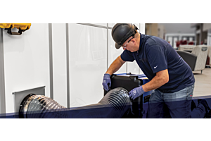 Un technicien en maintenance installe un conduit de ventilation sur un appareil de filtration HEPA devant une cloison modulaire blanche dans un établissement de soins de santé, illustrant les pratiques de confinement conformes à l’ÉRI 2.0.