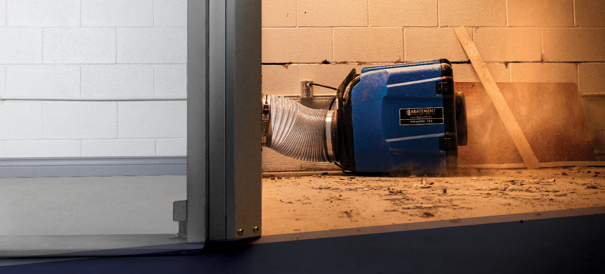 Abatement Technologies PREDATOR 750 air scrubber in action, exhausting dust and debris from a construction zone through a containment barrier. Demonstrates negative air pressure setup for effective dust control in renovation and remediation projects.