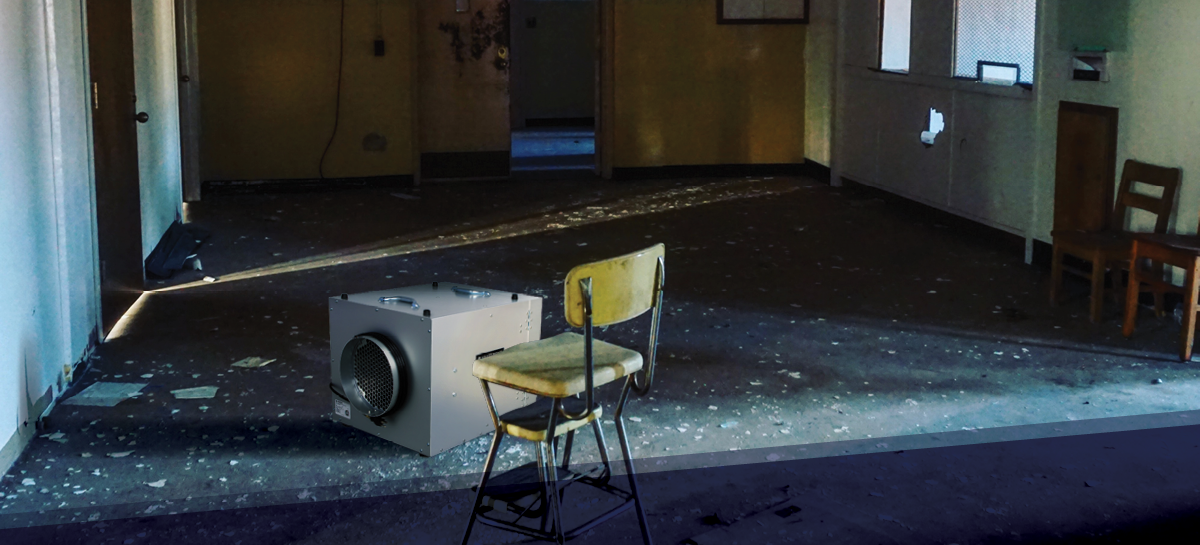 An abandoned room with peeling floors and scattered debris, illuminated by sunlight through a doorway. A HEPA air scrubber sits beside an old chair, highlighting restoration efforts in a damaged space.