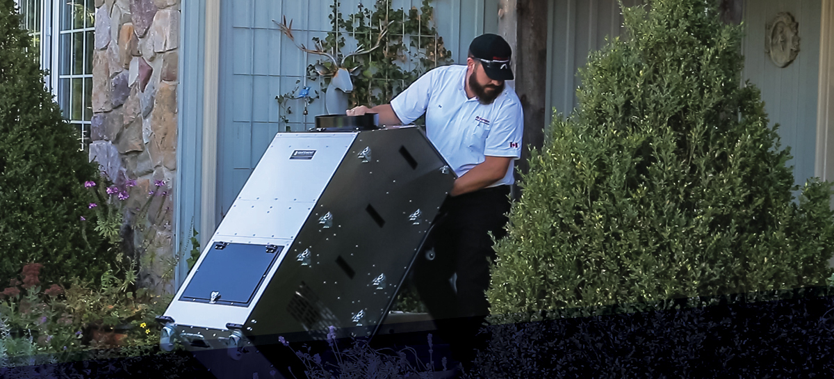 Technician using Abatement Technologies air filtration equipment outside a residential building, preparing for indoor environmental control or restoration work.