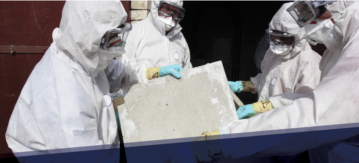 Travailleurs en combinaison de protection manipulant un panneau de matériau potentiellement dangereux lors d’un chantier de désamiantage ou de décontamination.