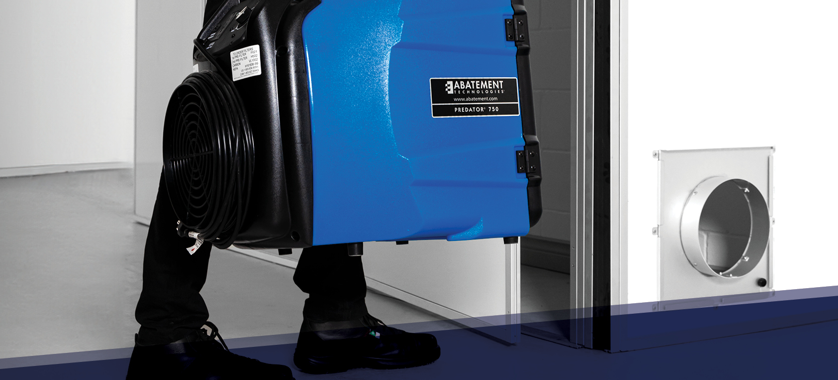 Technician transporting a PREDATOR 750 portable air scrubber by Abatement Technologies into a containment area. Used for negative air pressure applications, airborne particle control, and HEPA filtration in restoration and healthcare environments.